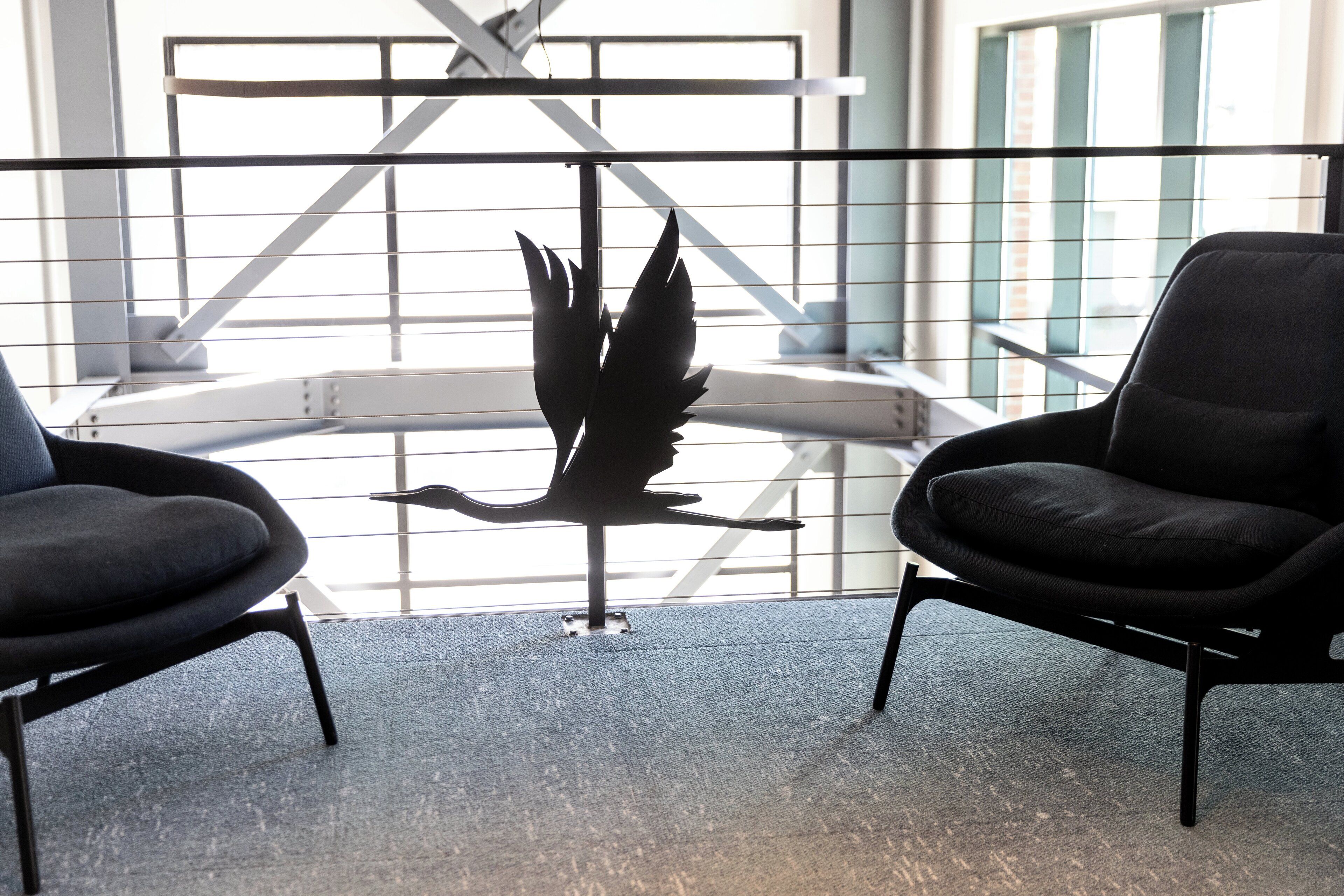A modern interior with two black chairs and a metal sculpture of a bird.