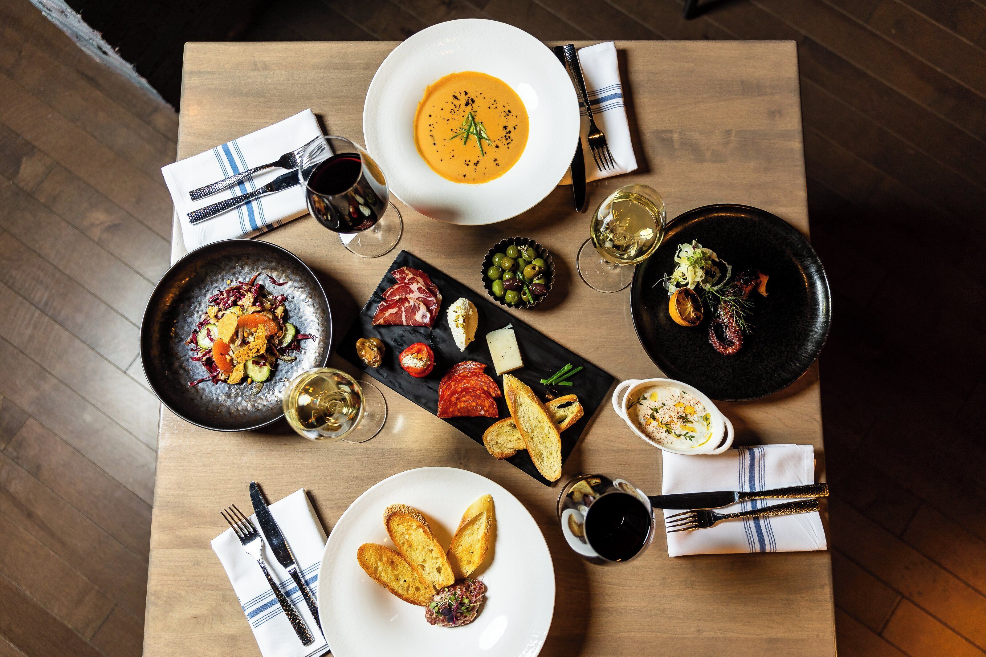 Una mesa de comedor con varios platos, entre ellos, un tazón de sopa, un plato de carne y un bol de aceitunas.