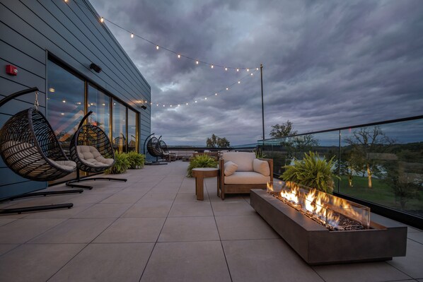 Une terrasse extérieure moderne, aménagée avec des sièges, un foyer et des guirlandes lumineuses.