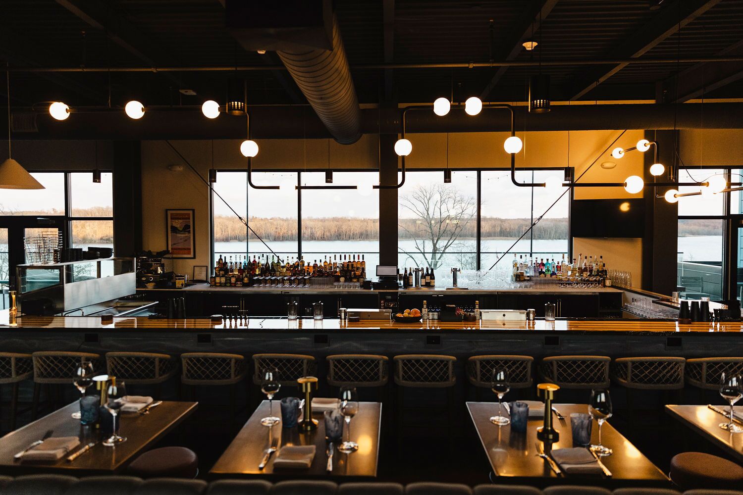 Un restaurante con zona de bar, ventanas amplias y vistas a un lago.