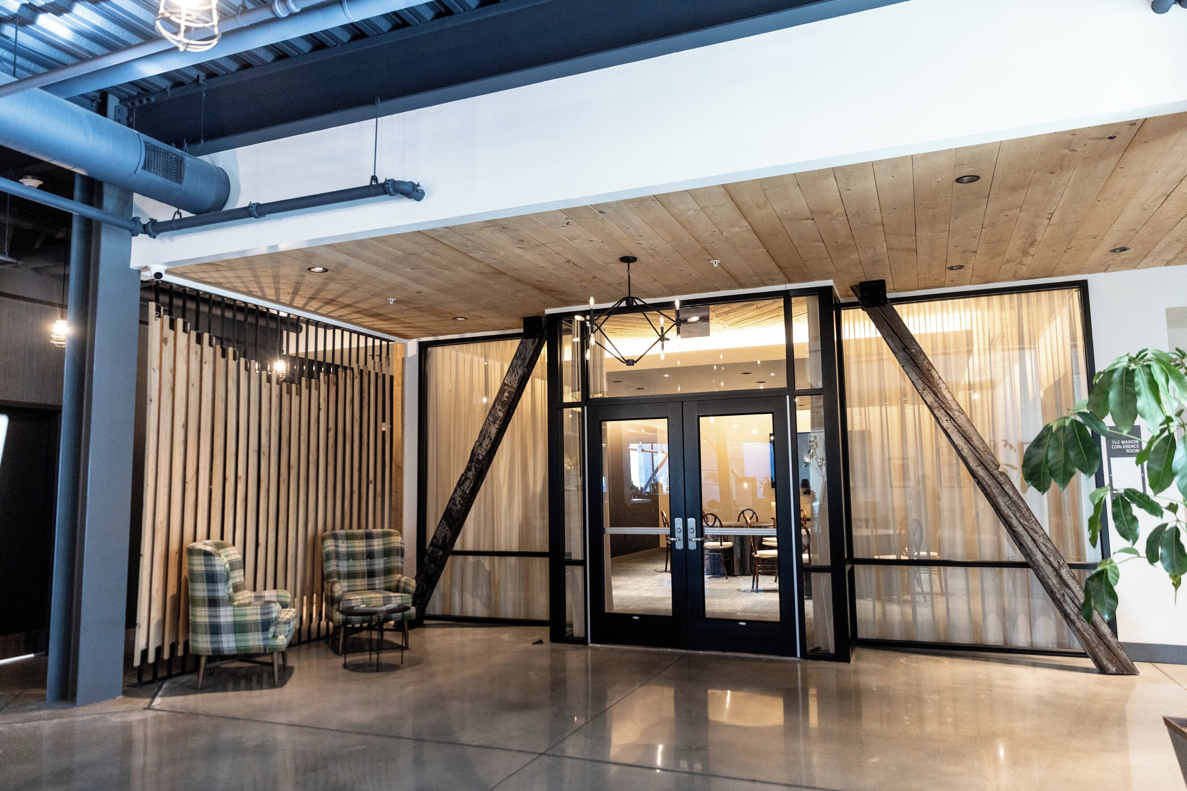 A modern interior with a wooden ceiling, glass doors leading to a dining area, and two plaid chairs by the entrance.