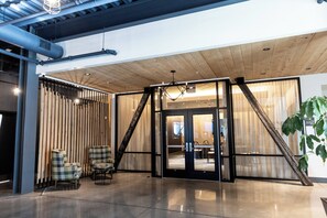 Un intérieur moderne avec un plafond en bois, des portes vitrées donnant sur un coin repas et deux fauteuils à carreaux près de l’entrée.