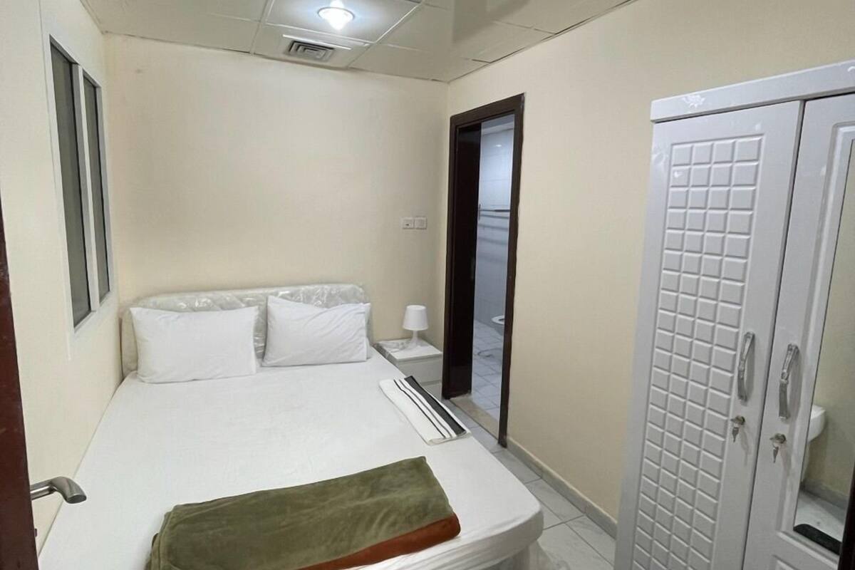 A small, clean room with a bed, a wardrobe, and a mirror.