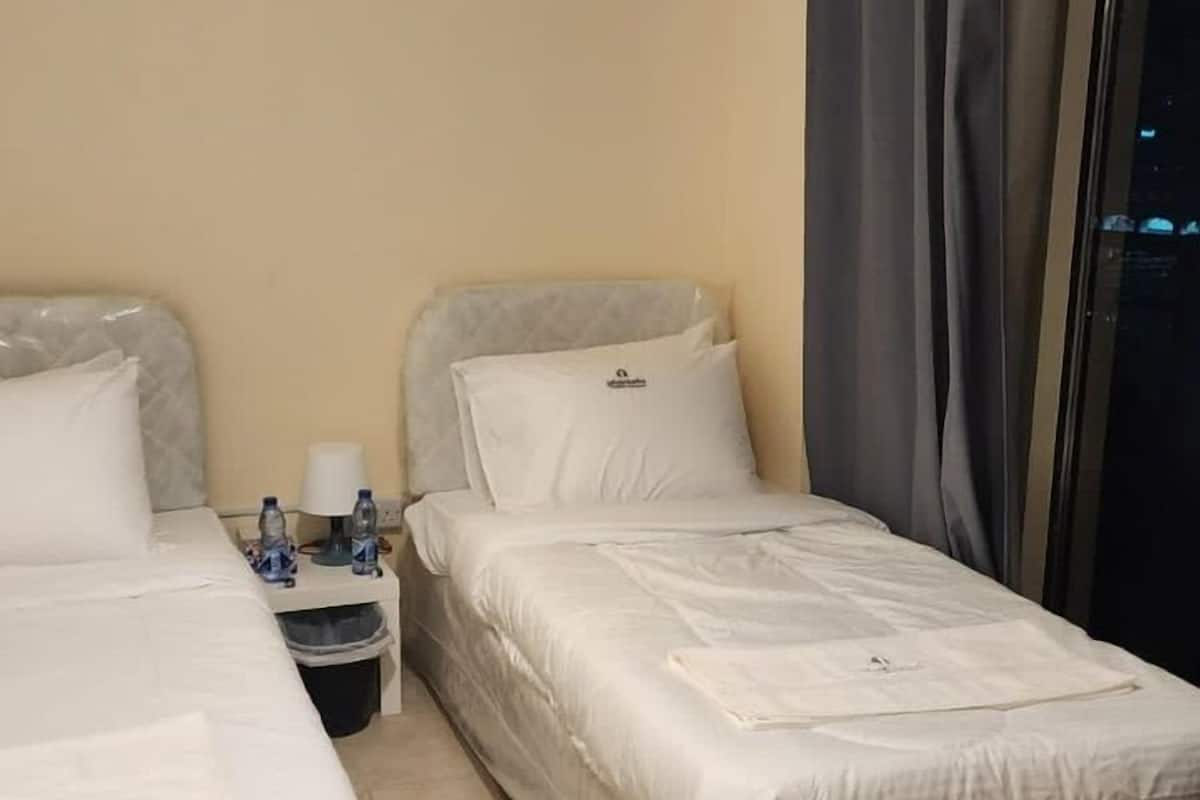 A hotel room with two beds, a nightstand with a lamp, and a window with curtains.