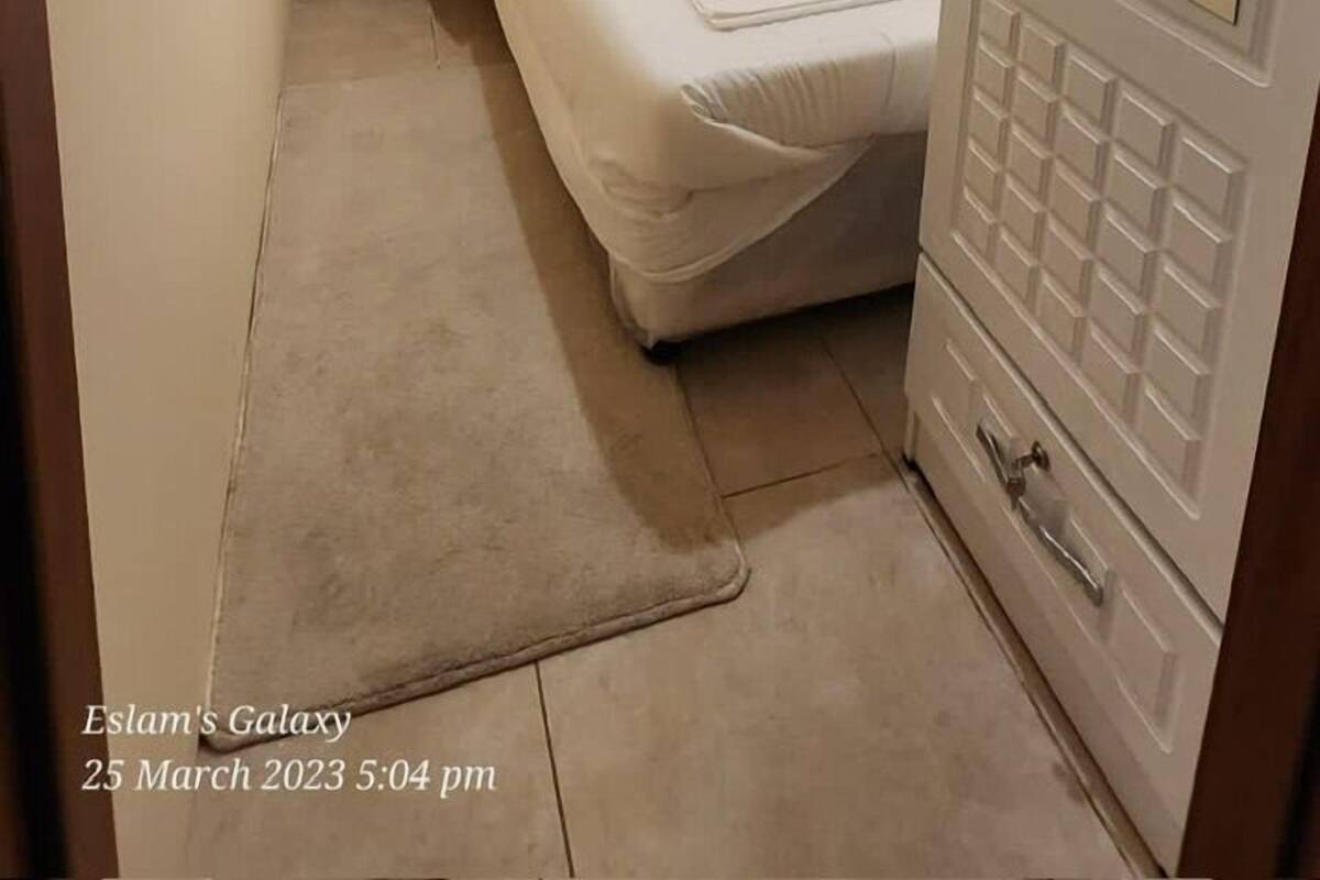 A narrow hotel room with a single bed, a bedside table, a lamp, and a wardrobe.
