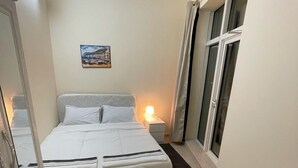 A small, neatly arranged bedroom with a bed, bedside table, lamp, and a window with curtains. - Pharaohs Inn Deira Hostel (Dubai)