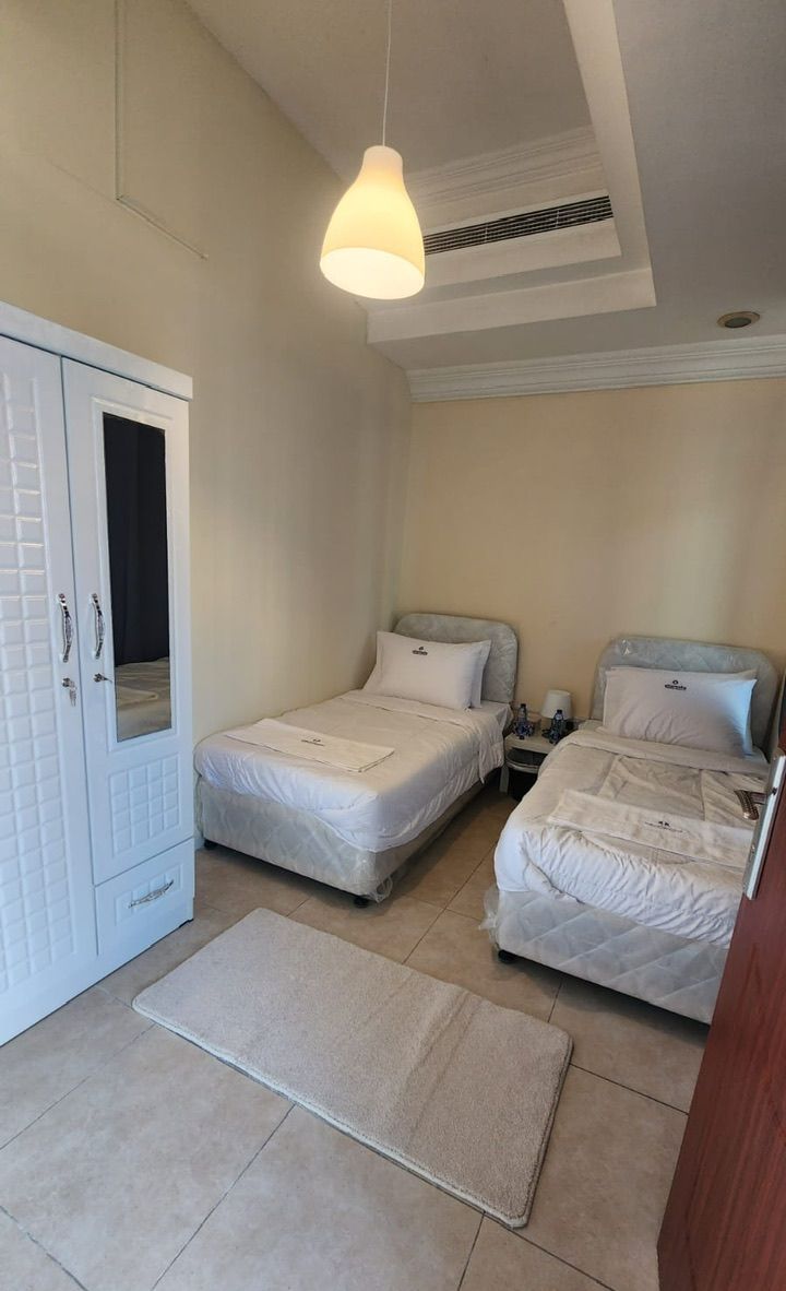 A small, clean room with two beds, a wardrobe, and a hanging light fixture.