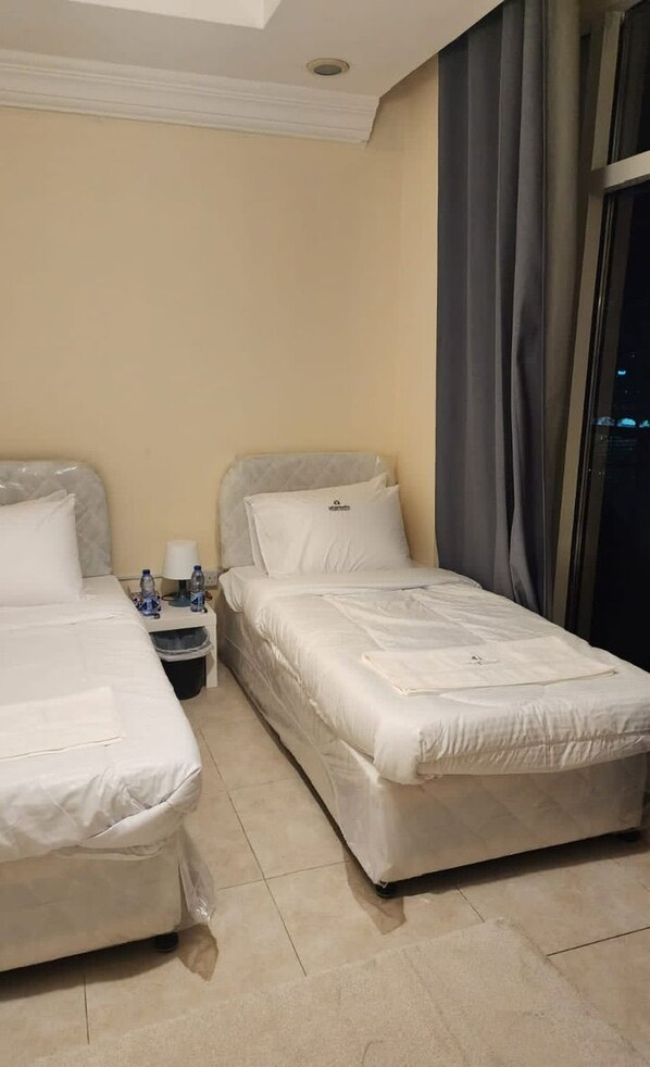 A hotel room with two beds, a nightstand with a lamp, and a window with curtains.
