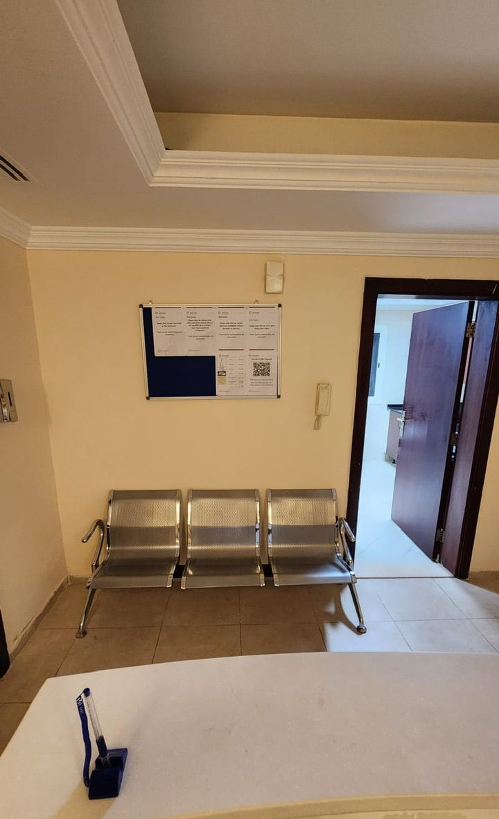 A waiting area with three metal chairs, a white table, and a bulletin board on the wall.