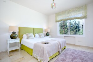 Ein Schlafzimmer mit einem Bett, zwei Nachttischen, einem Fenster mit Blick auf Bäume und einer Deckenleuchte.