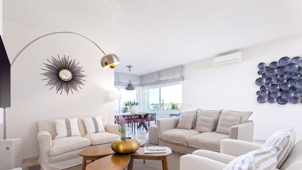Un salon avec deux canapés, une table basse et un téléviseur. On y trouve également un élément décoratif mural et un luminaire au plafond.