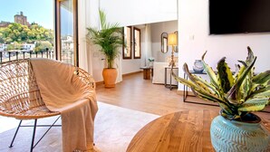 Ein modernes Wohnzimmer mit großem Fenster, einem Korbstuhl, einer Topfpflanze und einem Flachbildfernseher.