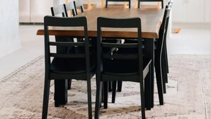 A modern dining area with a wooden table and black chairs, a chandelier, and a kitchen in the background. - Newly Renovated, Vintage Inspired, Large 4 BR Home (Mount Joy)