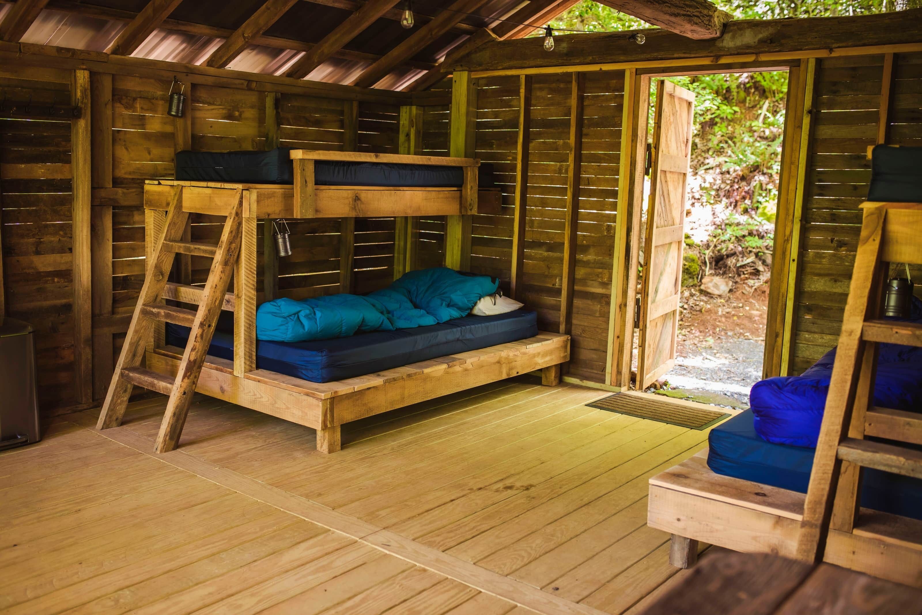 Une cabane en bois rustique, avec des lits superposés, une échelle et une petite table.