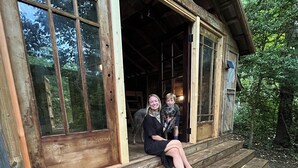 Een houten blokhut in landelijke stijl met een veranda, grote ramen en een zichtbaar interieur.