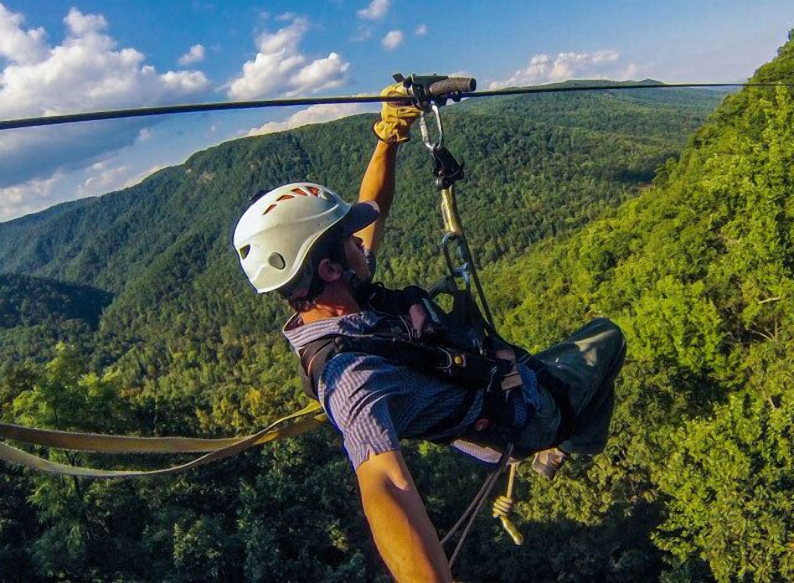 A person ziplining with a helmet and harness, overlooking a forested mountain landscape.