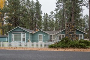 A row of green cabins with white trim, surrounded by a white picket fence, set in a forested area.
