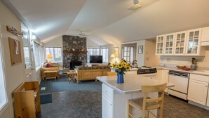 A spacious living area with a stone fireplace, a kitchen with white cabinets, and a dining area with wooden furniture. - Pine Street Cottage 3 BDRM home in a great location, near downtown Sisters (Sisters)
