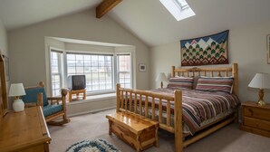A cozy bedroom with a sloped ceiling, a wooden bed, a small wooden table, a chair, a television, and a large window. - Pine Street Cottage 3 BDRM home in a great location, near downtown Sisters (Sisters)