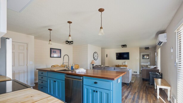 A kitchen with blue cabinets, a wooden countertop, and a dishwasher. There is a dining table and a bench in the adjacent dining area.