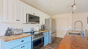 A kitchen with white cabinets, a wooden countertop, stainless steel appliances, and a wooden floor.