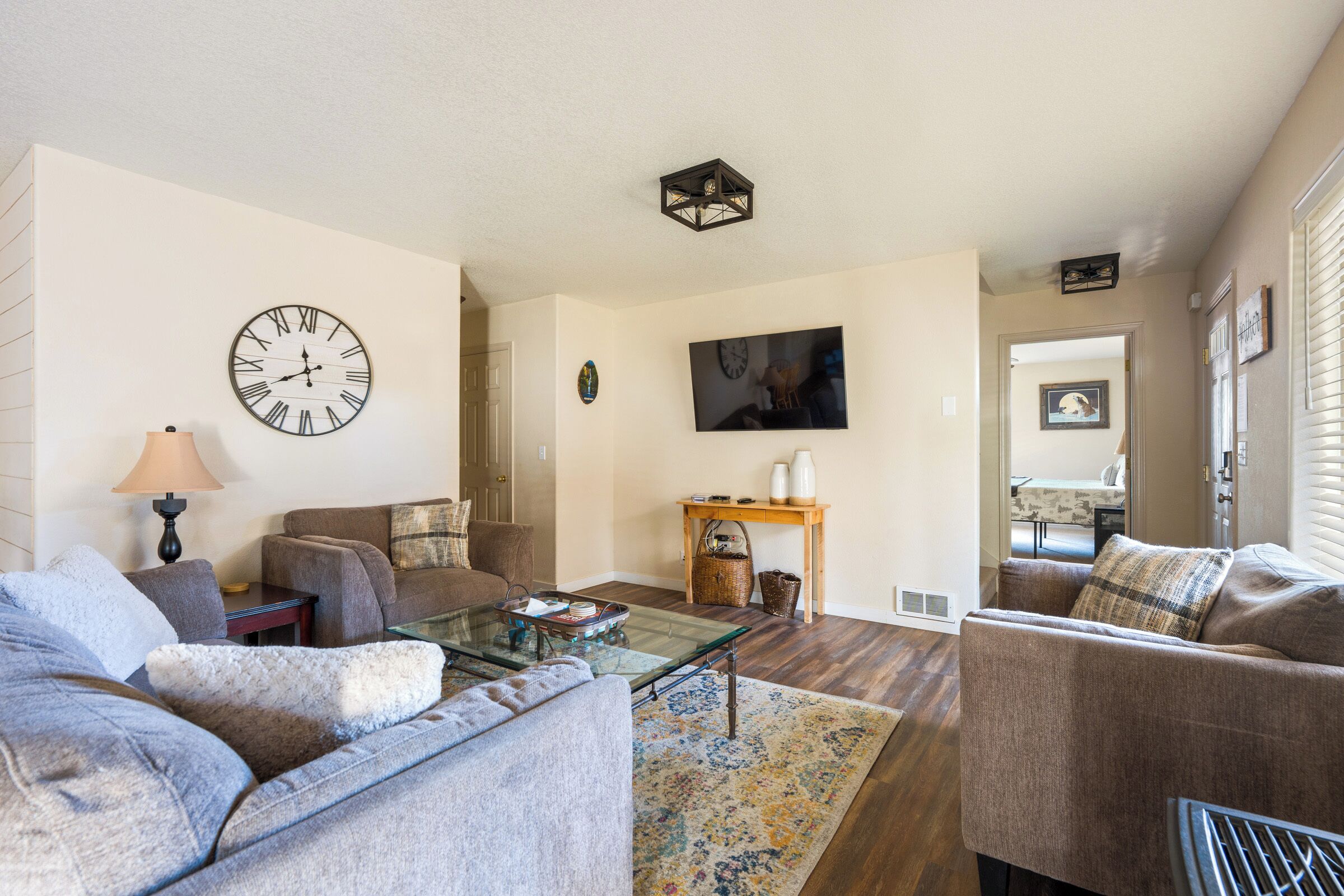A living room with a sofa, a coffee table, a clock, and a television.