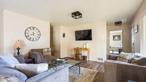 A living room with a sofa, a coffee table, a clock, and a television.