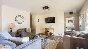 A living room with a sofa, a coffee table, a clock, and a television.