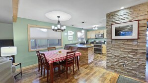 A spacious kitchen with wooden cabinets, a dining area with a red and white checkered tablecloth, and a stone accent wall. - Walk to Sisters | Hot Tub, Pool + Fireplace (Sisters)
