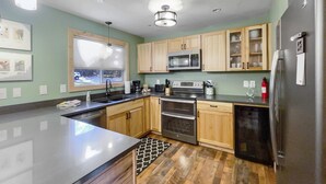 A modern kitchen with wooden cabinets, stainless steel appliances, and a large island. - Walk to Sisters | Hot Tub, Pool + Fireplace (Sisters)