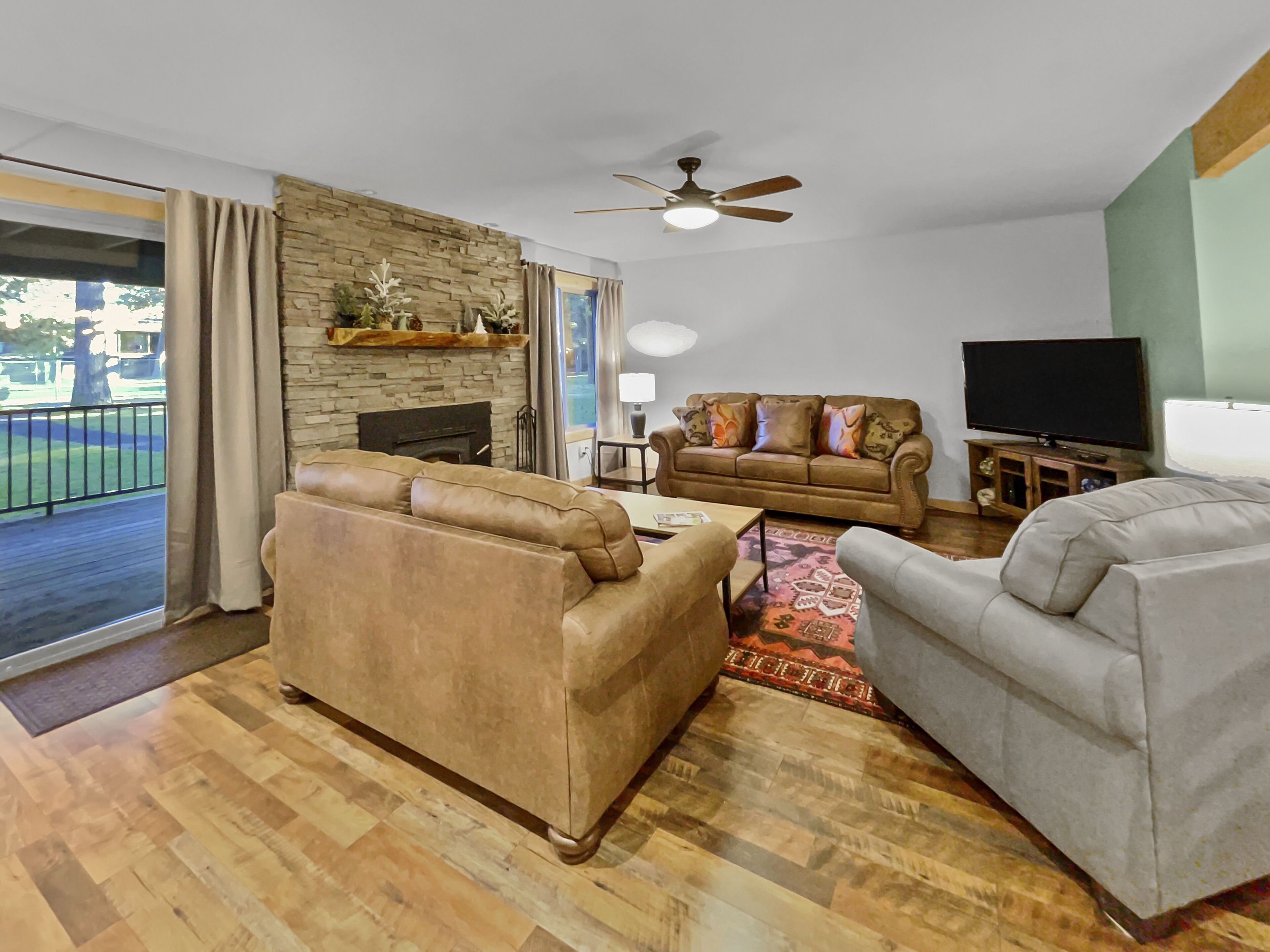 A living room with a fireplace, a sofa, a grey armchair, a TV, and a ceiling fan.