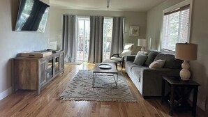 Een ruime woonkamer met een flatscreen-tv, een bank, een salontafel en een vloerkleed.