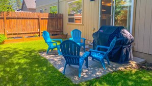 A backyard patio with outdoor furniture, a covered grill, and a wooden fence.