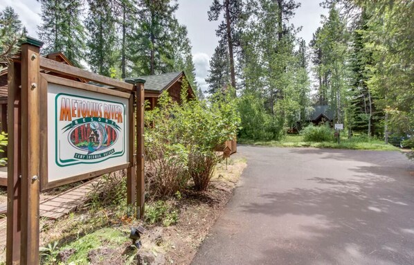 Señal de Metolius River Resort con una estructura tipo cabaña al fondo.