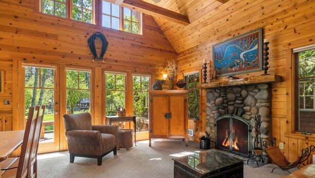 L’intérieur d’une cabane en rondins, avec une cheminée en pierre, des meubles en bois et de grandes fenêtres.