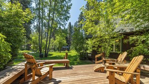 Une terrasse en bois, agrémentée de chaises Adirondack et d’une table de pique-nique, entourée d’une végétation luxuriante et de grands arbres.