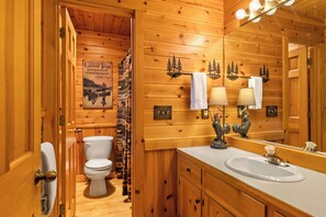Ein Badezimmer in einer Holzhütte mit Toilette, Waschbecken und einem Spiegel, der das Innere der Hütte reflektiert.