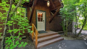 A wooden cabin with a front door, a wooden staircase, and a porch.
