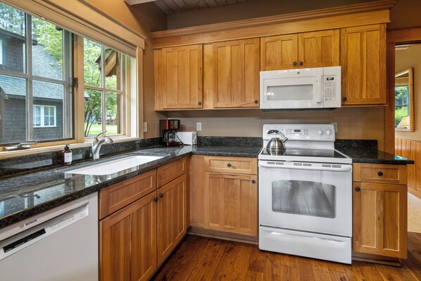 Una cocina con armarios de madera, un lavavajillas blanco Bosch, un horno blanco Bosch y un microondas blanco.