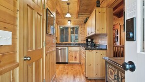 Une cuisine rustique, située dans une cabane en bois, équipée d’un lave-vaisselle, d’une machine à café et d’une fenêtre.