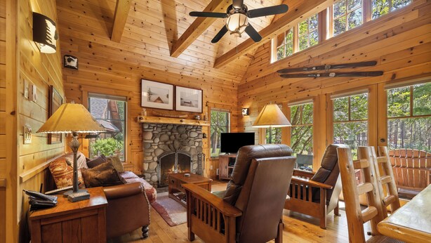 Un intérieur chaleureux de chalet en bois, avec une cheminée, des meubles en bois et de grandes fenêtres.