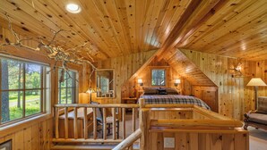 A log cabin interior with a loft bedroom, wooden walls, and a staircase.