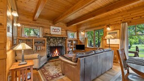 A cozy log cabin interior with a fireplace, leather sofa, wooden dining table, and a stone fireplace surround.