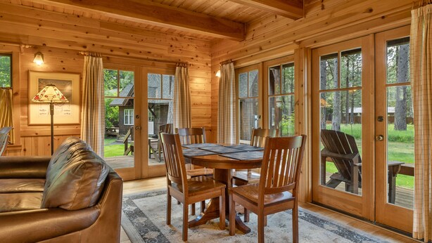 A wooden cabin interior with a dining table, chairs, and a leather couch.