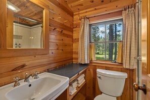 Baño de cabaña de madera con lavabo, inodoro y ventana con cortinas.