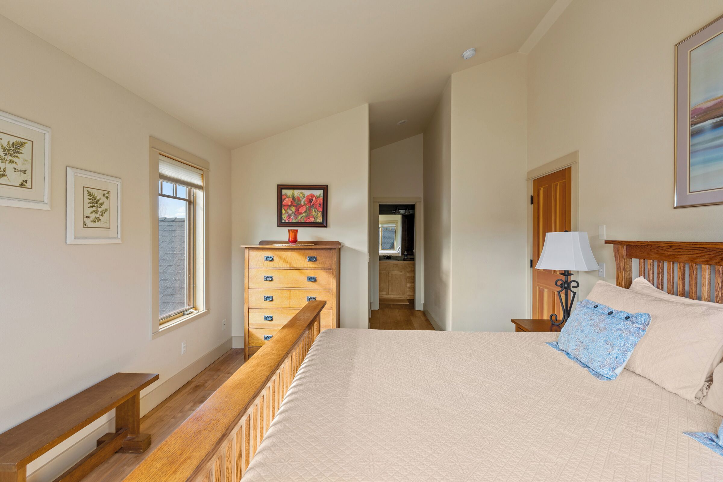 A bedroom with a bed, wooden bench, dresser, and framed pictures on the wall.