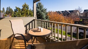 A balcony with a wooden table and chairs, a view of a residential street, and houses in the background. - Pool access | Shared hot tub | Walk to town (Sisters)