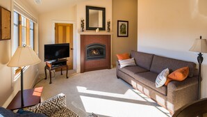 A living room with a fireplace, a sofa, a television, and a lamp. - Pool access | Shared hot tub | Walk to town (Sisters)