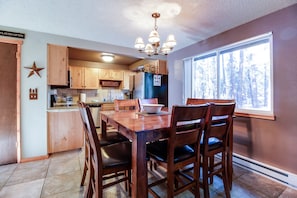 A kitchen with wooden cabinets, a dining table with chairs, a chandelier, and a window with a view of trees.