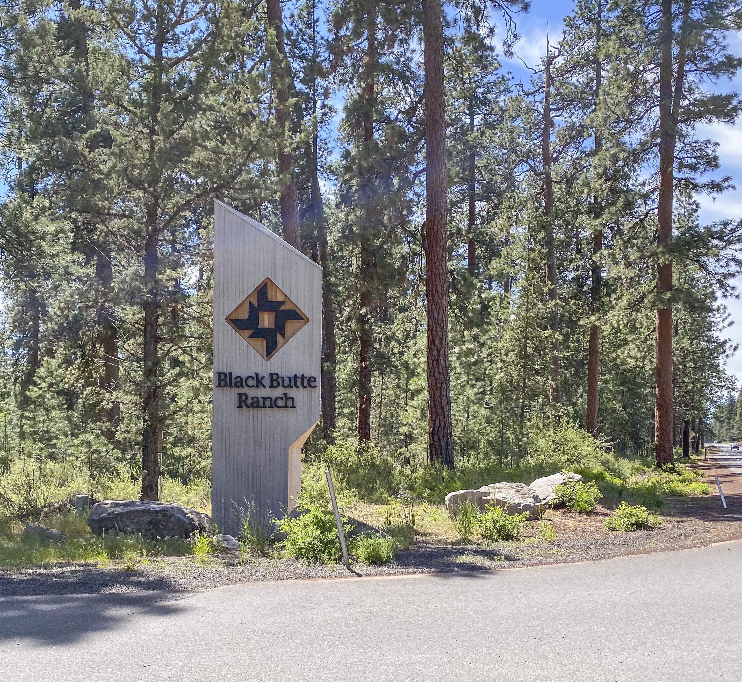 Un panneau indiquant l’emplacement de Black Butte Ranch, avec un logo en forme de losange, entouré de grands pins.